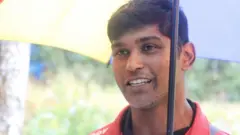 වැසි වැටෙන අවස්ථාවක කුඩයක් ඉහලා ගෙන සිනහමුසු මුහුණින් සිටින බදුල්ල දිස්ත්‍රික්කයට අයත් ලුණුගල නගරය වසම අයත් ග්‍රාම නිලධාරී ආර්.එම්.ඩී නිශාන්තගේ ඡායාරූපයක් මෙහි දැක්වේ.