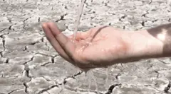 පොළව ඉරිතලාගිය පසුබිමක පුද්ගලයකුගේ අතට ජලය වැටෙන අයුරු දැක්වේ.