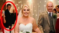 A happy bride and groom walking back up the aisle after their wedding, with beaming smiles on their faces. Many of the guests are applauding them. Andrew Hillhouse can be seen in the background as one of the attendees, with a red ring overlain on the image to draw the eye to him.