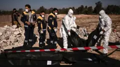 أفراد من (الخوذ البيضاء) ينقلون أكياس جثث تحتوي على رفات بشرية تم انتشالها من مقبرة جماعية في دمشق