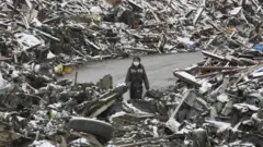 Uma mulher caminha entre os escombros na cidade japonesa de Minamisanriku, no norte do Japão, após o tsunami de 2011.