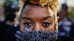 A woman with "BLM" written on her cheek poses during a demonstration