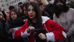 A young protester with red ink on her face that spells "HELP" cuts her hair with scissors during a demonstration against the death of Mahsa Amini on September 23, 2022 in Berlin, Germany