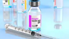una botella con la vacuna contra el herpes zóster junto a una jeringa