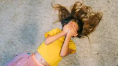 Niña en el suelo con la cara tapada