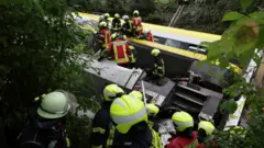 An overturned train carriage is attended by emergency service personnel