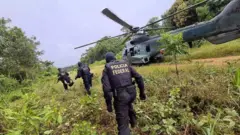Foto mostra agentes da PF se aproximando de um helicóptero em uma área de floresta na Terra Indígena Yanomami, em Roraima