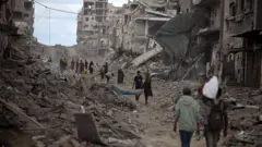 Palestinos caminham por uma rua coberta de escombros