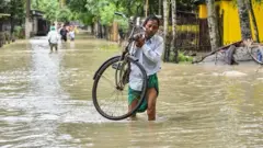 A man carries his bicycle as he wades through flood waters in Solmara of Nalbari district, in India's Assam state on June 19, 2022