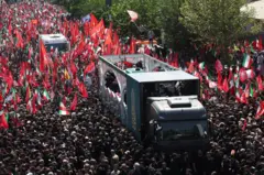 سيارة ضخمة تحمل نعوش المرشد الأعلى الإيراني الراحل آية الله علي خامنئي وأفراد عائلته، تشق طريقها وسط موكب جنائزي حاشد تعلوه الأعلام الحمراء في طهران، إيران، في 6 يوليو/تموز 2026، وقد نُثرت عليها الورورد

