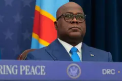 Perezida wa Repubulika ya Demokarasi ya Congo Félix Tshisekedi yicaye asa n'ureba hejuru, yambaye ikositimu y'uburu na karuvati y'ubururu n'ishati y'umweru. Kuri kositimu ye hariho akabendera gato ka Congo naho inyuma ye hari ibendera rinini rya Congo. Yambaye indorerwamo n'agakoresho ko kumvisha (écouteur) mu gutwi kumwe. Ifoto yafotorewe i Washington DC, muri Amerika, ku itariki ya 4 Ukuboza (12) mu 2025, mu muhango wo gusinya amasezerano y'amahoro hagati ye na Perezida w'u Rwanda Paul Kagame (utaboneka ku ifoto).