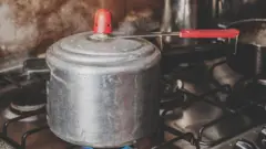 Panela de pressão de alumínio, no fogão, com fogo ligado e soltando vapor