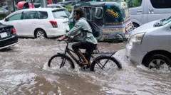 Carros e um homem em uma bicicleta no meio de um alagamento
