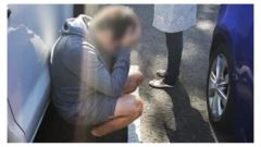 A suspect in custody kneels down and holds his head
