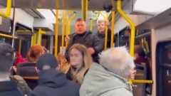 Зображення зсередини трамваю, на передньому плані чоловік і жінка, чоловік обернувся назад, за ним двоє чоловіків, які очевидно щось йому говорять, у трамваї багато інших пасажирів 