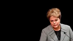 Dilma com olhar um pouco sériob1 bet site oficialpé, dianteb1 bet site oficialmicrofone e fundo preto