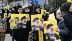 Lebanese citizens carry Hezbollah flags and posters of Hassan Nasrallah as residents begin returning to their homes in the southern Lebanese town of Aitaroun following Israel's withdrawal from several areas.