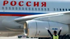 Крупным планом самолет с надписью «Россия», перед ним сотрудник аэропорта жестикулирует.