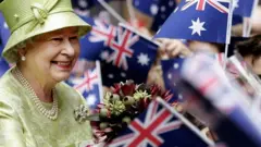 The Queen receives flowers from waiting school children with waiving national flags after the Commonwealth Day Service in Sydney, Australia