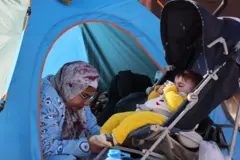 نازحة لبنانية في خيمة وطفل يجلس في عربته أمامها