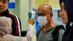 A passenger has his body temperature checked by a health official at Sultan Iskandar Muda International Airport near Banda Aceh in Indonesia