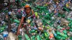 Una mujer en medio de botellas de plástico para reciclar.
