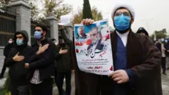 متظاهر يحمل لافتة ورقية رسمت عليها صورتا محسن فخري زادة وقاسم سليماني قائد فيلق القدس الإيراني الذي اغتالته الولايات المتحدة في شهر يناير الماضي بالعراق