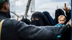 A member of the Syrian Democratic Forces (SDF) stands before veiled women at al-Hol camp