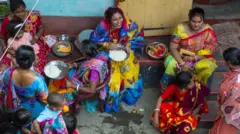 節慶期間，身著色彩鮮豔紗麗的印度教婦女坐在達卡的一個庭院裡，吃著米飯和西瓜