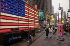 Pessoas andam pelas ruas de Nova York, em meio a uma enorme bandeira americana
