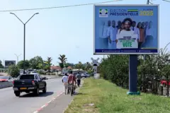 Des personnes passent devant un panneau d'affichage appelant les citoyens gabonais à voter lors de la prochaine élection présidentielle à Libreville, le 7 avril 2025.