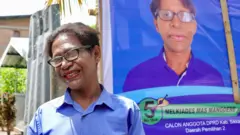 Mami Vera berpose tersenyum di depan baliho kampanyenya