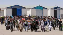 Afghan refugees walk with their belongings after being deported back from Iran at the Islam Qala Border between Afghanistan and Iran, in Herat province on 30 May 2024