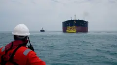 Сотрудник порта смотрит на нефтяной танкер, пришвартованный в море у нефтяного терминала