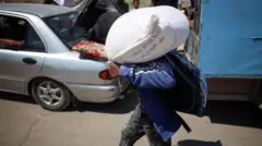 Um homem carrega um saco de farinha nas costas enquanto caminha com outros pela rua