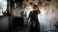 Concepción García em pé no meio de um cômodo destruído pelo fogo, onde se veem o teto e as paredes escurecidos e carbonizados.
