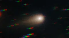 O cometa 3I/Atlas exibido na forma de núcleo brilhante, rodeado por uma coroa nebulosa e uma cauda à esquerda. Ao fundo, filas de pontos azuis, verdes e vermelhos, representando estrelas que se movem em relação ao cometa.