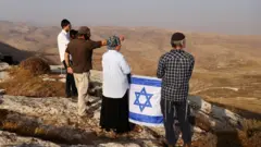 مستوطنون يحملون العلم الإسرائيلي خلال مهمة استكشافية للعثور على أراض جديدة بالقرب من مستوطنة كوخاف هاشاهار الإسرائيلية في الضفة الغربية التي تحتلها إسرائيل، 6 نوفمبر/تشرين الثاني 2022.