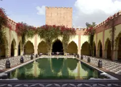Piscina al aire libre rodeada de terraza cubierta con arcos de estilo marroquí.