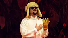 Bad Bunny cantando sobre un escenario durante su residencia en Puerto Rico luciendo un gorro esquimal, gafas oscuras y un solo guante.