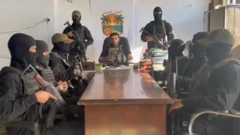 Ashraf Mansi lee una declaración frente a hombres armados vestidos de oscuro y sentados frente a una mesa de madera el 14 de octubre de 2025.