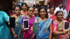 Mulheres beneficiárias do programa Mukhyamantri Ladaki Bahin Yojana mostram seus celulares com a mensagem de confirmação da chegada do dinheiro do programa em Kisan Nagar, Thane, Índia.