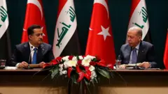 Irak Başbakanı Muhammed Şiya el-Sudani ve Cumhurbaşkanı Recep Tayyip Erdoğan birbirine bakıyor. Arkada Türkiye ve Irak bayrakları var