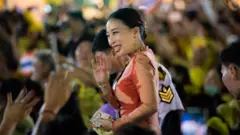Thailand's Princess Bajrakitiyabha waves to the crowd while a bodyguard in white stands behind her