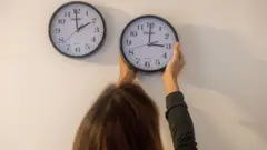 Bir kadın iki ayrı saate bakıyor ve birini ileriye alıyor