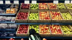 Puesto de frutas en un supermercado en Caracas. Se ve a una niña agarrando a una manzana.