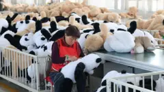 Uma mulher em uma fábrica costura pandas de brinquedo fofinhos
