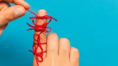 Mão com um dos dedos cheio de laços de fio vermelho para relembrar coisas