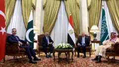 Hakan Fidan ve Pakistan, Mısır ve Suudi Arabistanlı mevkidaşları Kahire toplantısında koltuklarda oturmuş halde ve her bir ülkenin bayrağı önünde poz veriyor