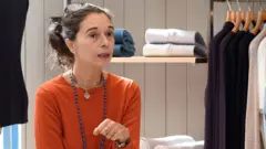 Orsola de Castro é uma mulher branca. Ela está usando uma blusa laranja e colares. Ela está com cabelo preso.